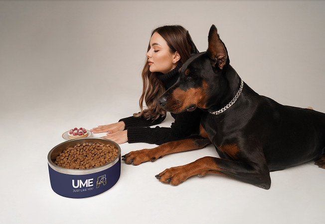 A woman with a Doberman lying down next to UME food and a cake